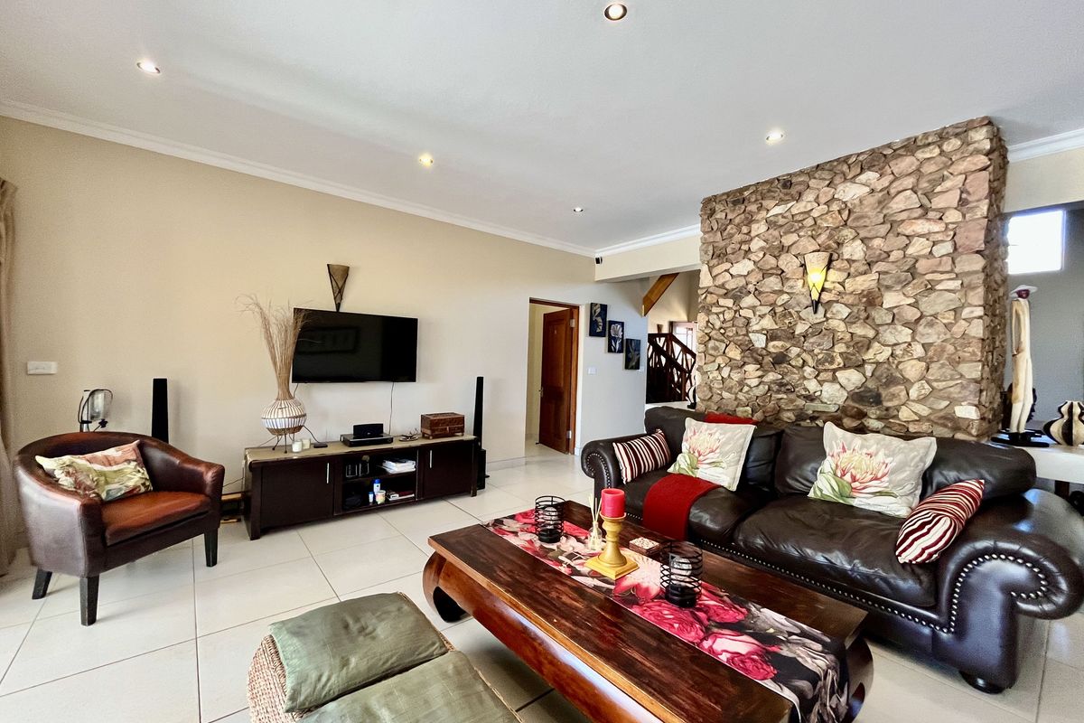 Spacious living room featuring a prominent natural stone feature wall, tiled flooring, and recessed downlighting.