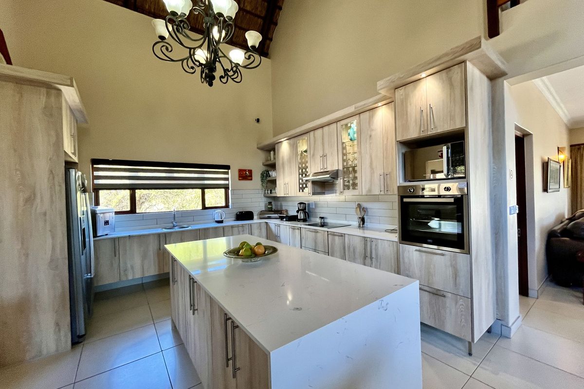 Modern kitchen featuring light wood cabinetry, stone countertops, a central island, built-in oven, and high vaulted ceilings with exposed thatch detail.