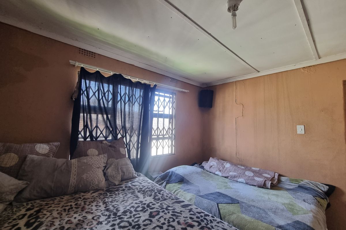 A bedroom featuring a window with security bars, basic electrical fixtures, and visible wall cracks requiring maintenance and cosmetic updates.