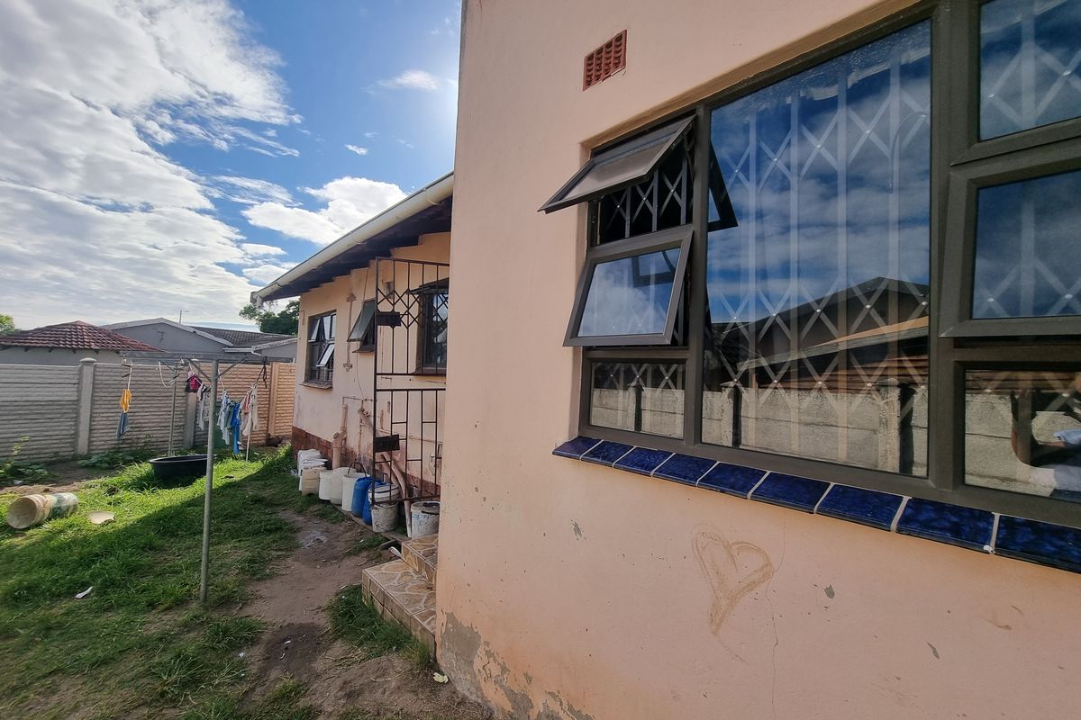 Side view of the house exterior showing metal security window bars, tiled window sills, and a small garden area with a washing line.