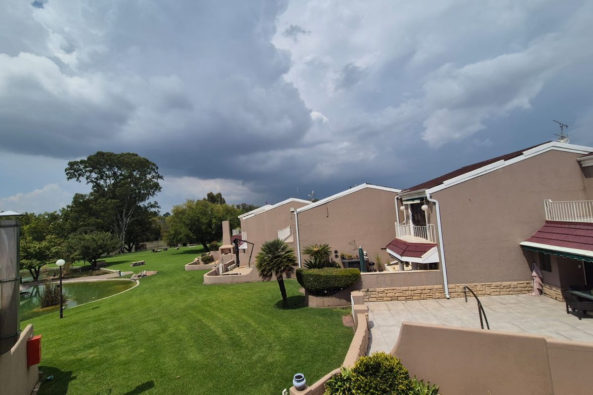 View of the rear exterior of the townhouse complex, featuring private paved patios, landscaped communal lawns, and a tranquil pond area.