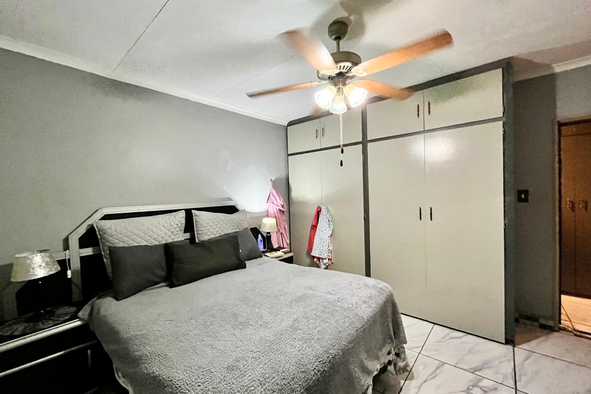 A bedroom featuring built-in cupboards, tiled flooring, and a ceiling fan, providing a functional sleeping space.