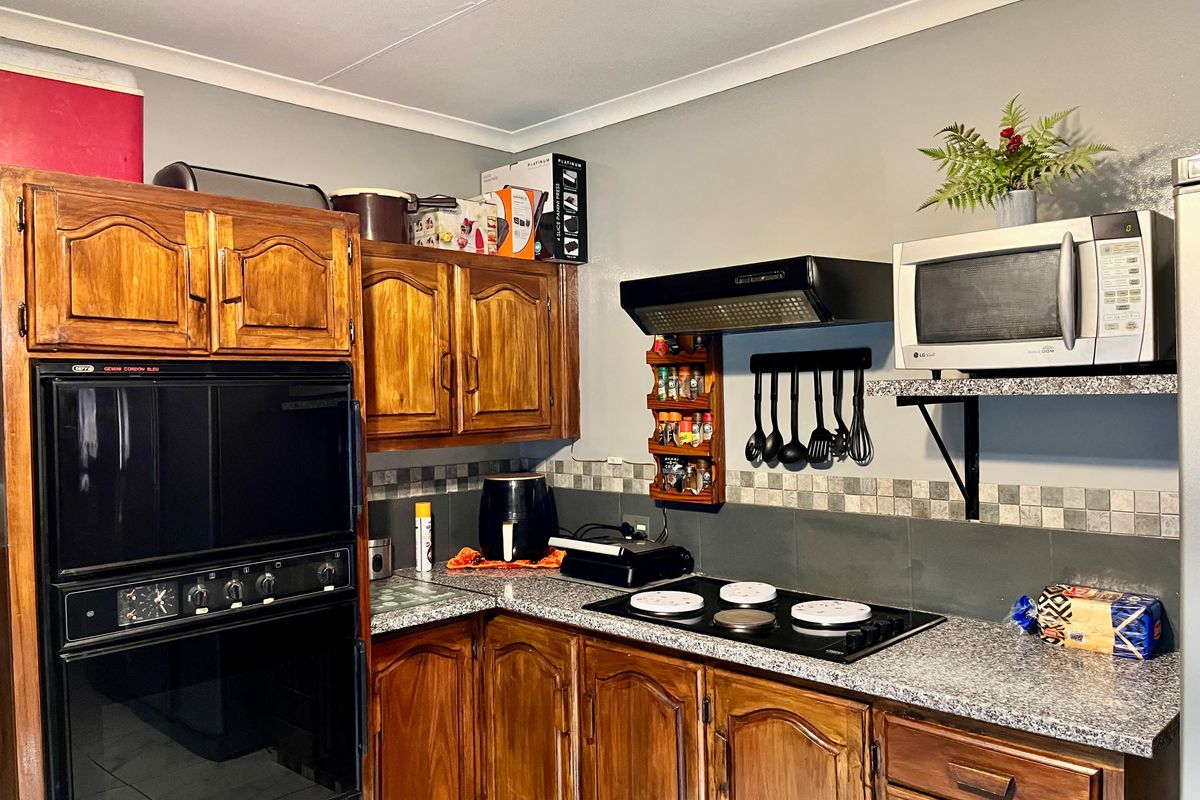 A functional kitchen featuring wooden cabinetry, granite-look countertops, a built-in oven, and a black electric hob with an extractor fan.