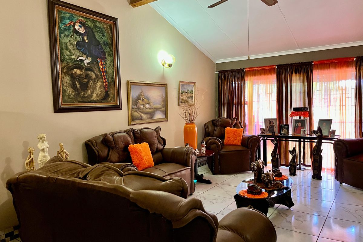 Spacious living room featuring vaulted ceilings, exposed timber beams, a ceiling fan, and polished floor tiles with large windows allowing natural light.
