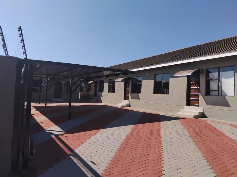 Exterior view of an apartment complex featuring a paved driveway, covered carport parking, and secure perimeter electric fencing.