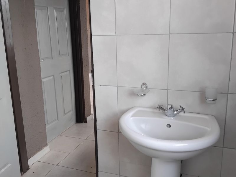 A clean bathroom featuring a white pedestal basin with chrome fixtures, complemented by neutral ceramic wall and floor tiling.