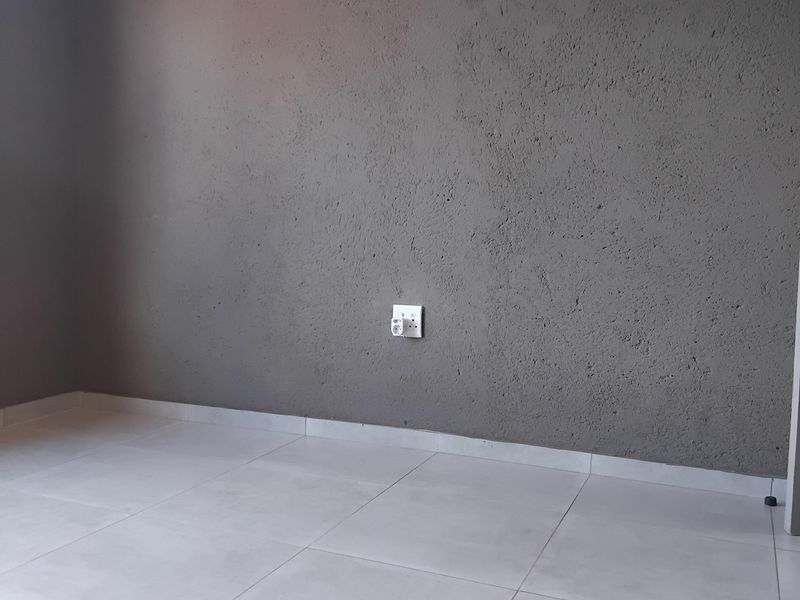 An empty bedroom featuring modern grey textured walls, light-colored ceramic floor tiles, and clean white skirting boards.