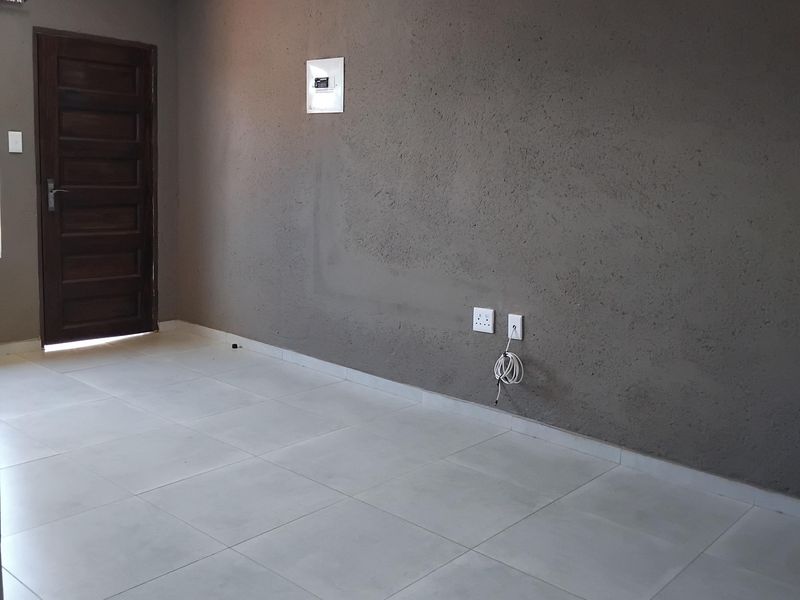 An empty living area featuring light-colored floor tiles, a dark textured feature wall, and a solid timber entrance door.