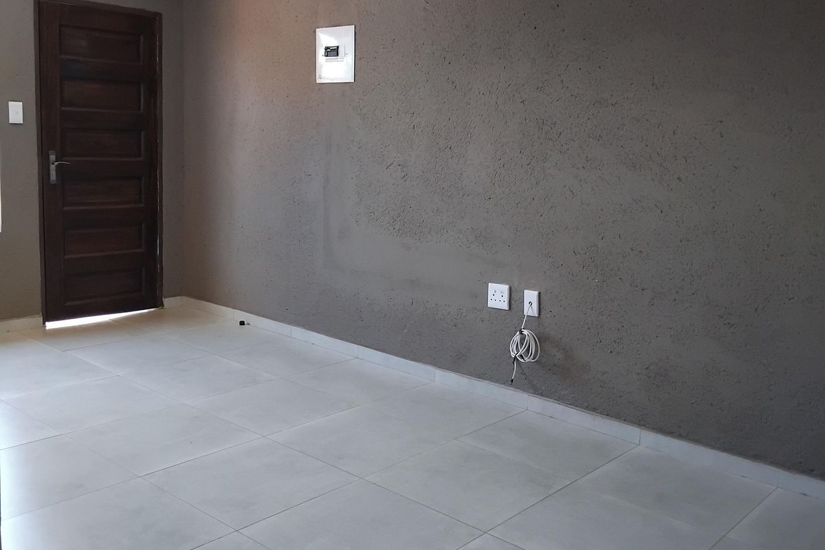 An empty living area featuring light-colored floor tiles, a dark textured feature wall, and a solid timber entrance door.