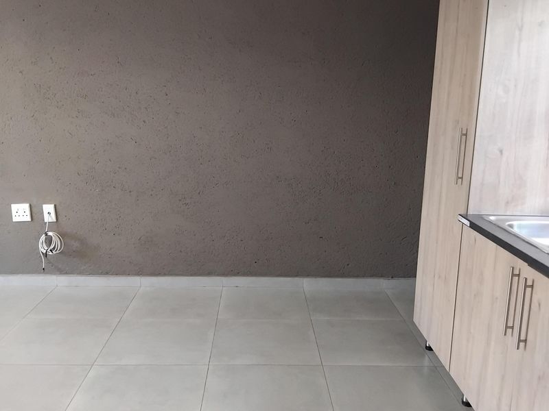 A clean, empty kitchen area featuring modern light wood cabinetry, tiled flooring, and a textured feature wall.