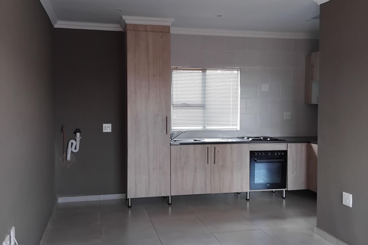 A clean, empty kitchen featuring light wood-finish cabinetry, a built-in oven and hob, tiled splashback, and neutral floor tiles.