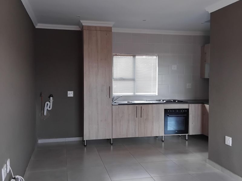 A clean, empty kitchen featuring light wood-finish cabinetry, a built-in oven and hob, tiled splashback, and neutral floor tiles.