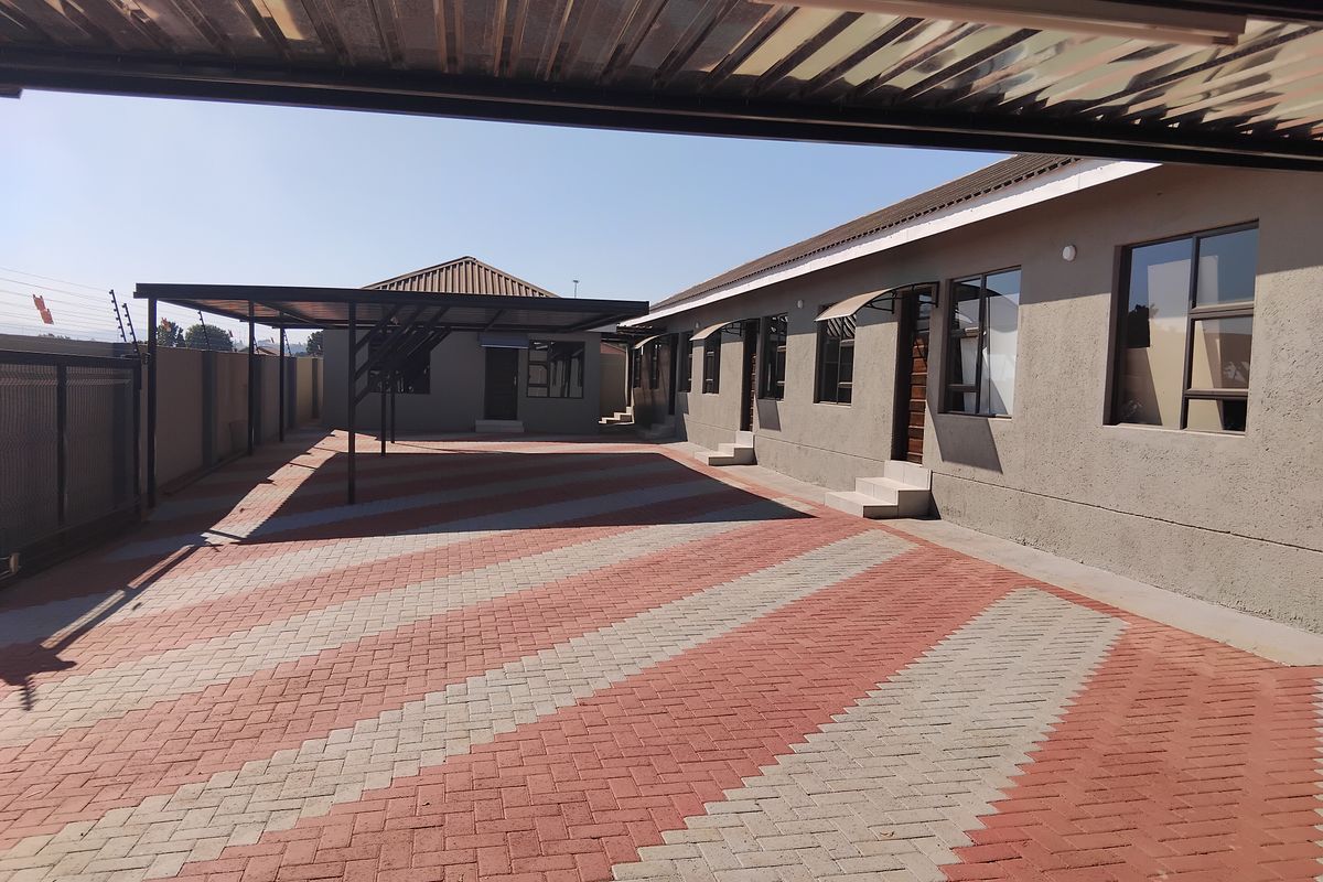 Spacious paved courtyard area featuring a covered carport, secure perimeter fencing, and well-maintained exterior building facades.
