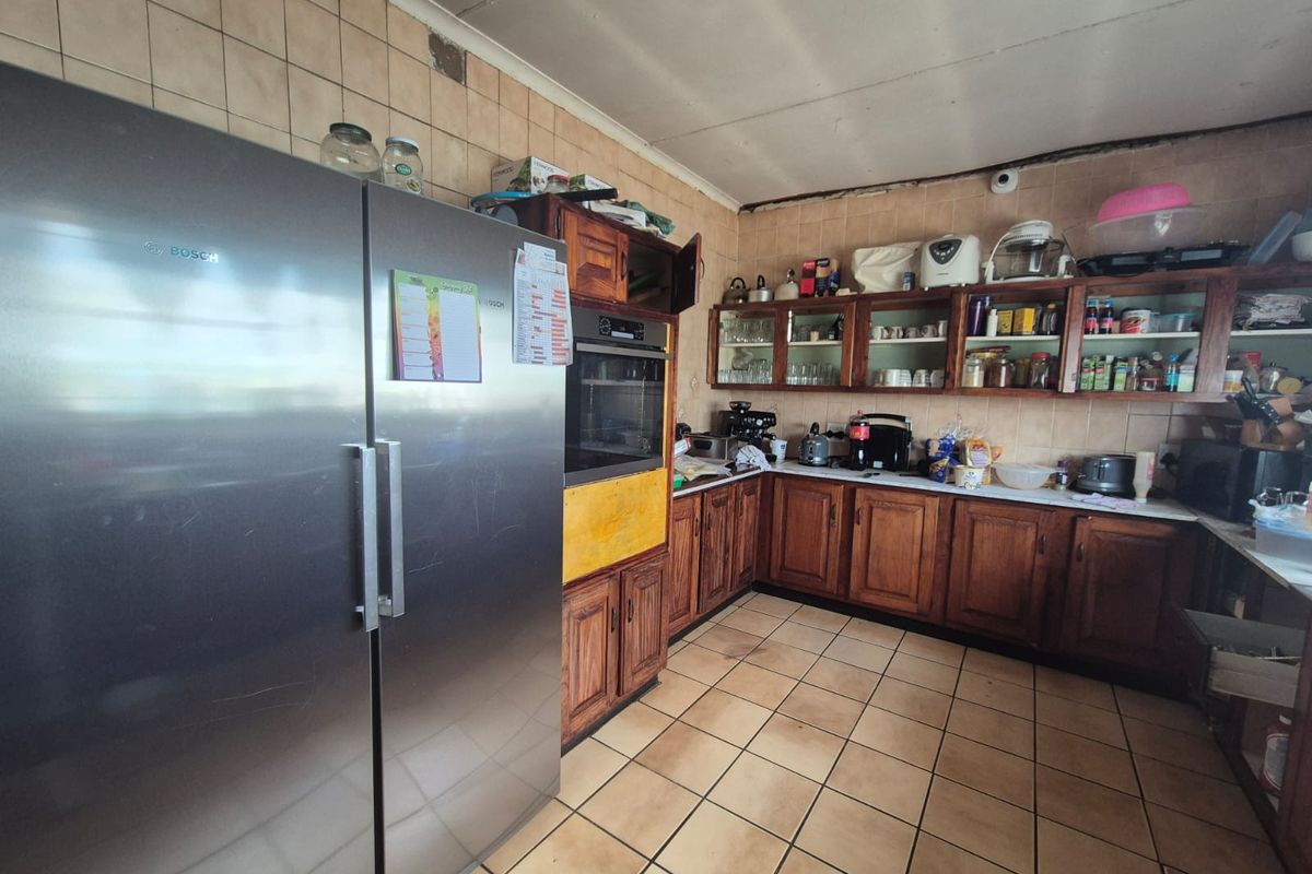 A dated kitchen featuring wooden cabinetry, tiled flooring, and wall-mounted storage, offering a functional layout with potential for modern renovation.