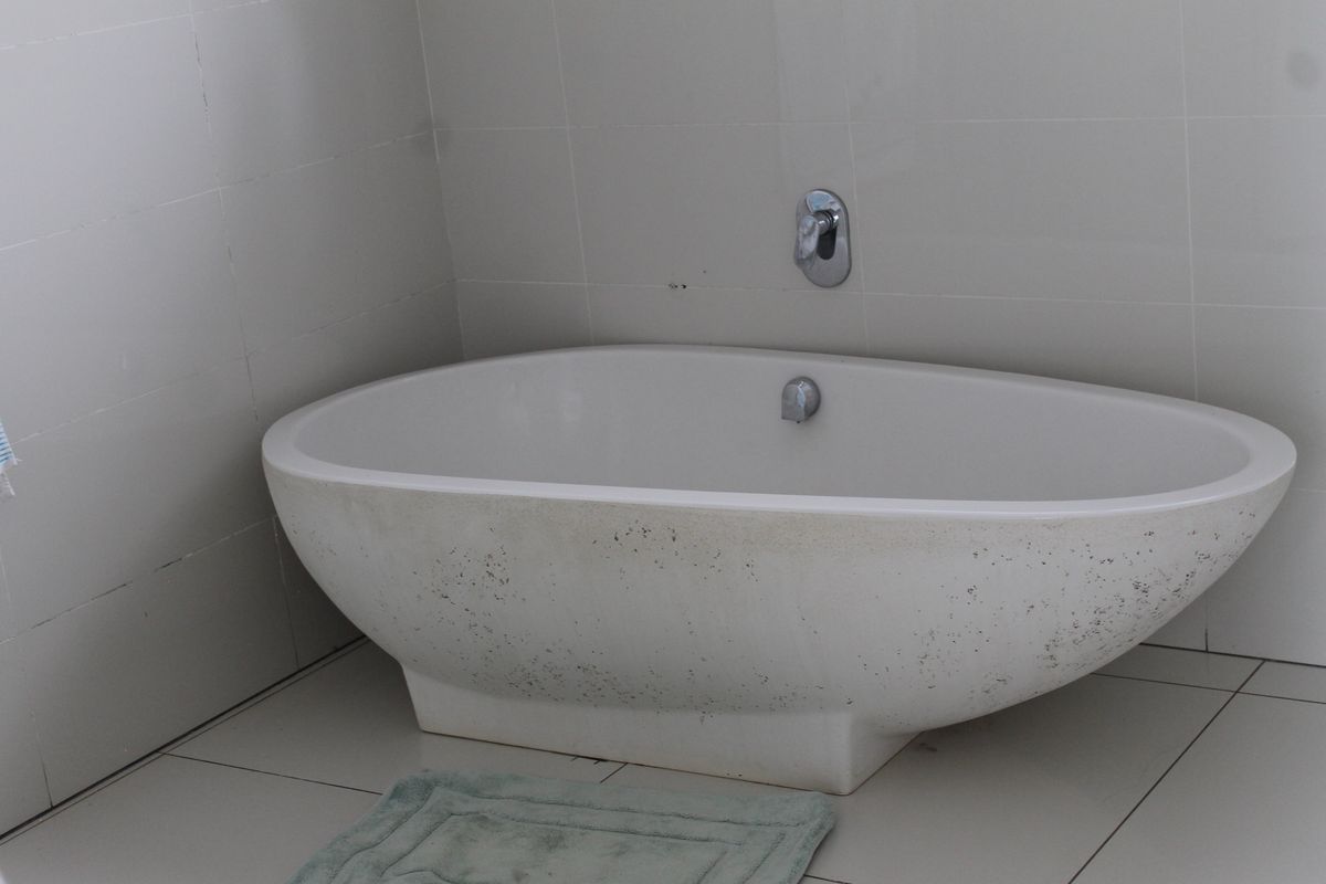 A bathroom featuring a freestanding bathtub with wall-mounted chrome faucet fixtures and neutral ceramic wall and floor tiling.
