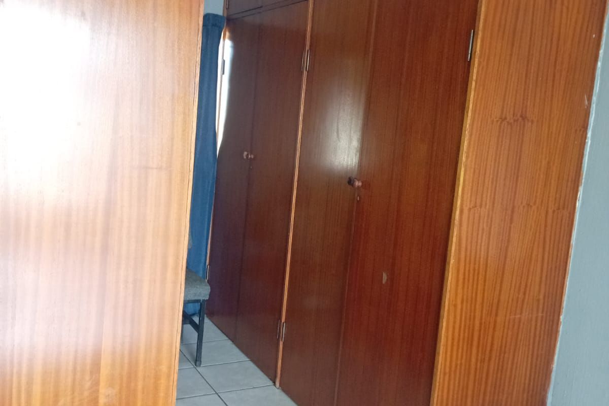 A bedroom featuring floor-to-ceiling built-in wooden cupboards and tiled flooring, offering ample storage space.