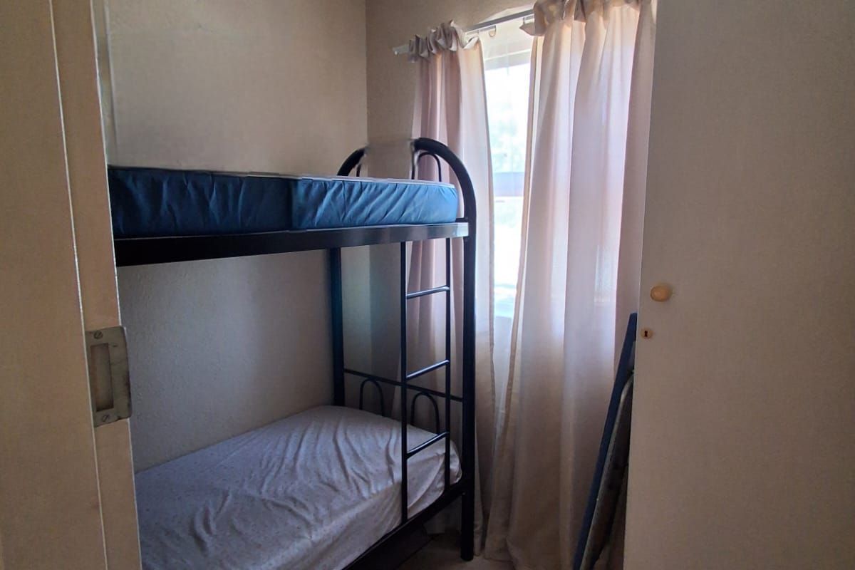 A compact bedroom featuring tiled flooring, a window with curtain tracks, and a built-in cupboard.