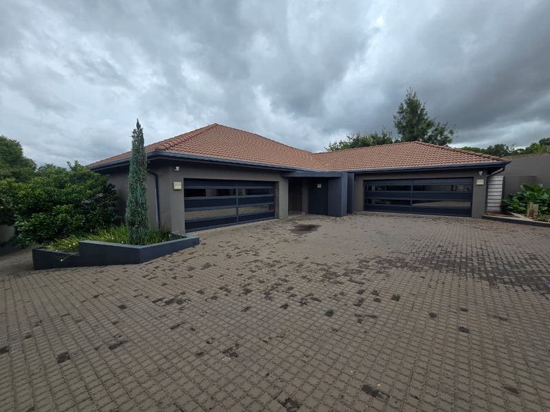 Front exterior view of the property featuring a spacious paved driveway and a double garage with modern dark-toned doors.