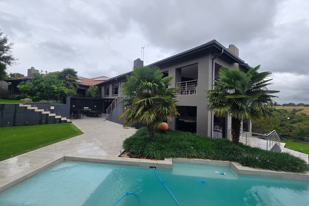 Rear view of the property featuring a swimming pool, expansive tiled patio, landscaped garden, and a multi-level structure with a balcony.