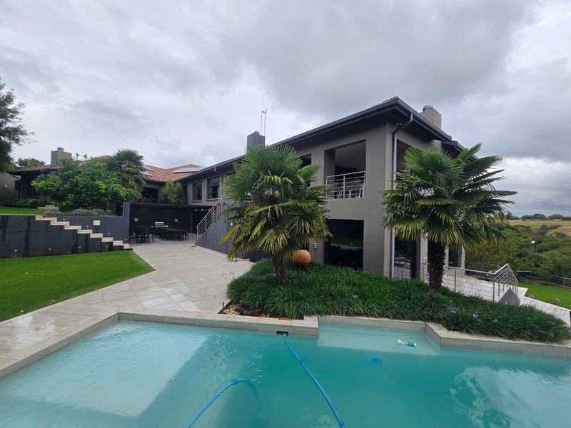 Rear view of the property featuring a swimming pool, expansive tiled patio, landscaped garden, and a multi-level structure with a balcony.