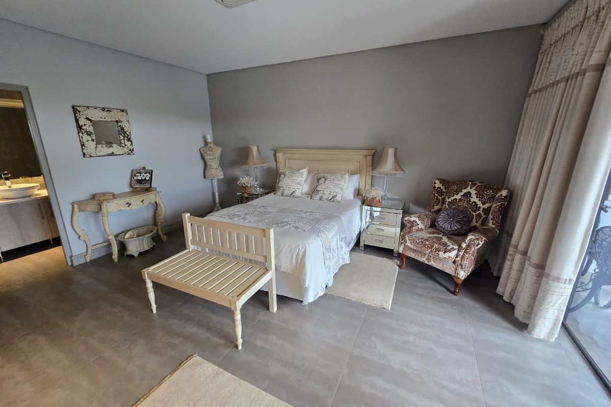 Spacious bedroom featuring neutral tiled flooring, recessed ceiling lighting, and direct access to an en-suite bathroom and outdoor area through sliding glass doors.