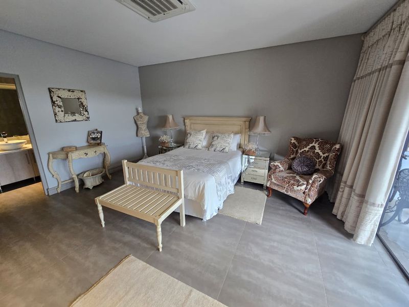 Spacious bedroom featuring neutral tiled flooring, recessed ceiling lighting, and direct access to an en-suite bathroom and outdoor area through sliding glass doors.