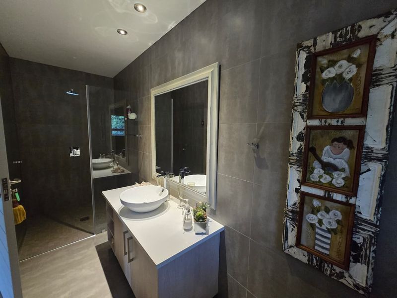 Modern bathroom featuring a sleek vanity with a vessel sink, large wall mirror, and a spacious walk-in shower with contemporary grey wall tiling.