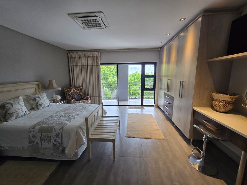 Spacious bedroom featuring built-in cupboards, a vanity area, recessed lighting, ceiling-mounted air conditioning, and direct access to a private balcony through sliding glass doors.