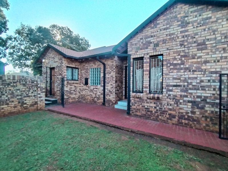 Rear view of a face brick house featuring a paved patio area, security bars on windows, and a private garden space.