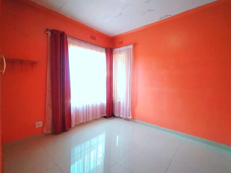An empty bedroom featuring tiled flooring and corner windows, providing a blank canvas for potential interior design updates.