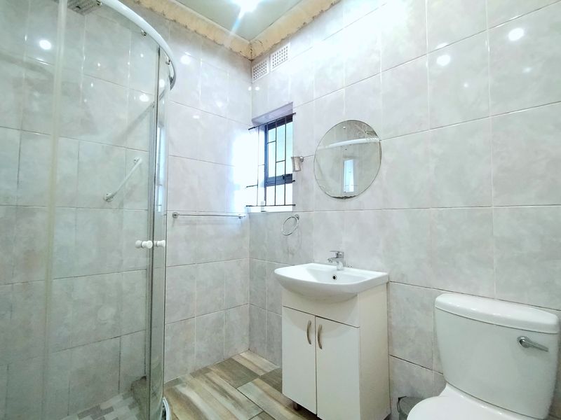 A functional bathroom featuring a glass shower enclosure, vanity basin, and toilet, finished with neutral wall tiles and wood-look floor tiles.