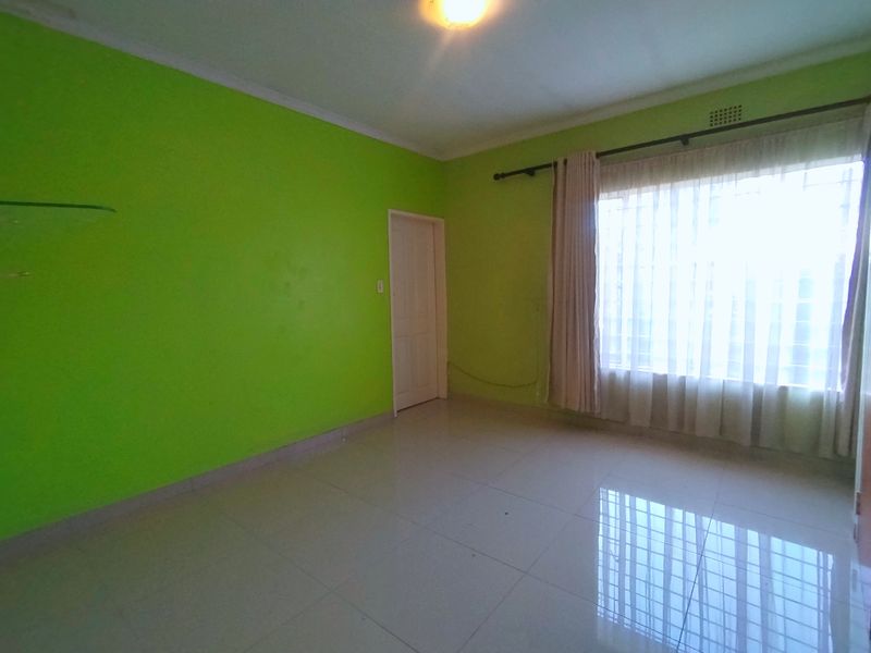 An empty bedroom featuring tiled flooring, bright green walls, and a large window with a curtain rod.