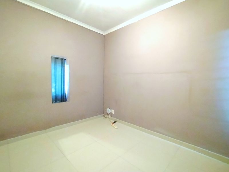 A vacant bedroom featuring neutral tiled flooring, cove cornicing, and a small window, providing a blank canvas for personalization.