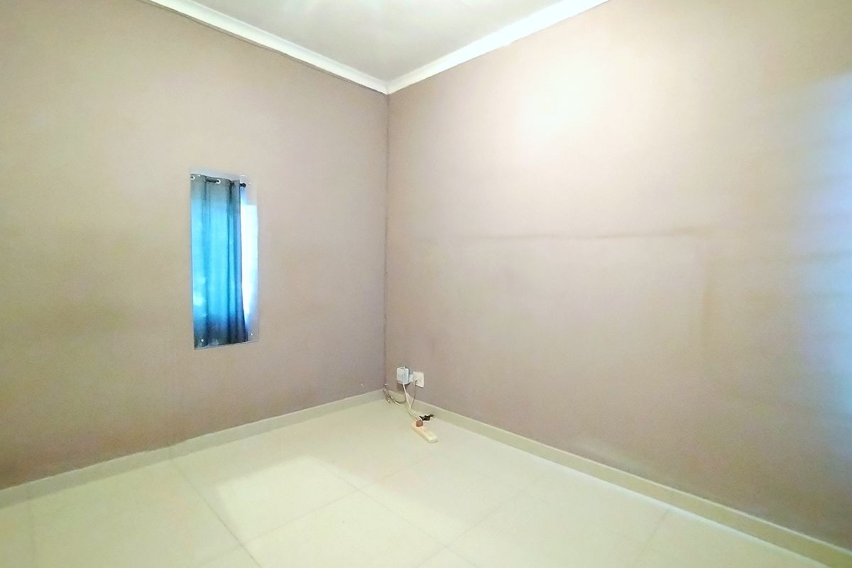 A vacant bedroom featuring neutral tiled flooring, cove cornicing, and a small window, providing a blank canvas for personalization.