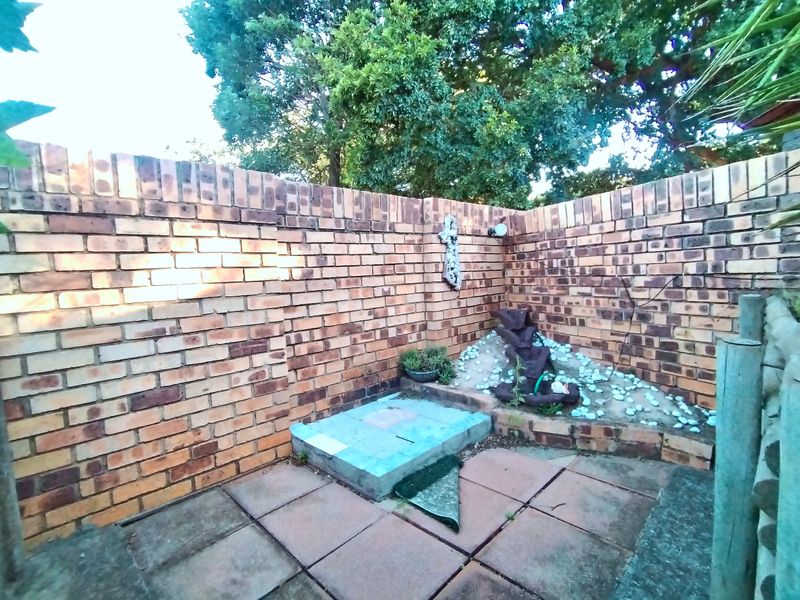 A private garden corner featuring a brick boundary wall, paved flooring, and a decorative stone water feature area.