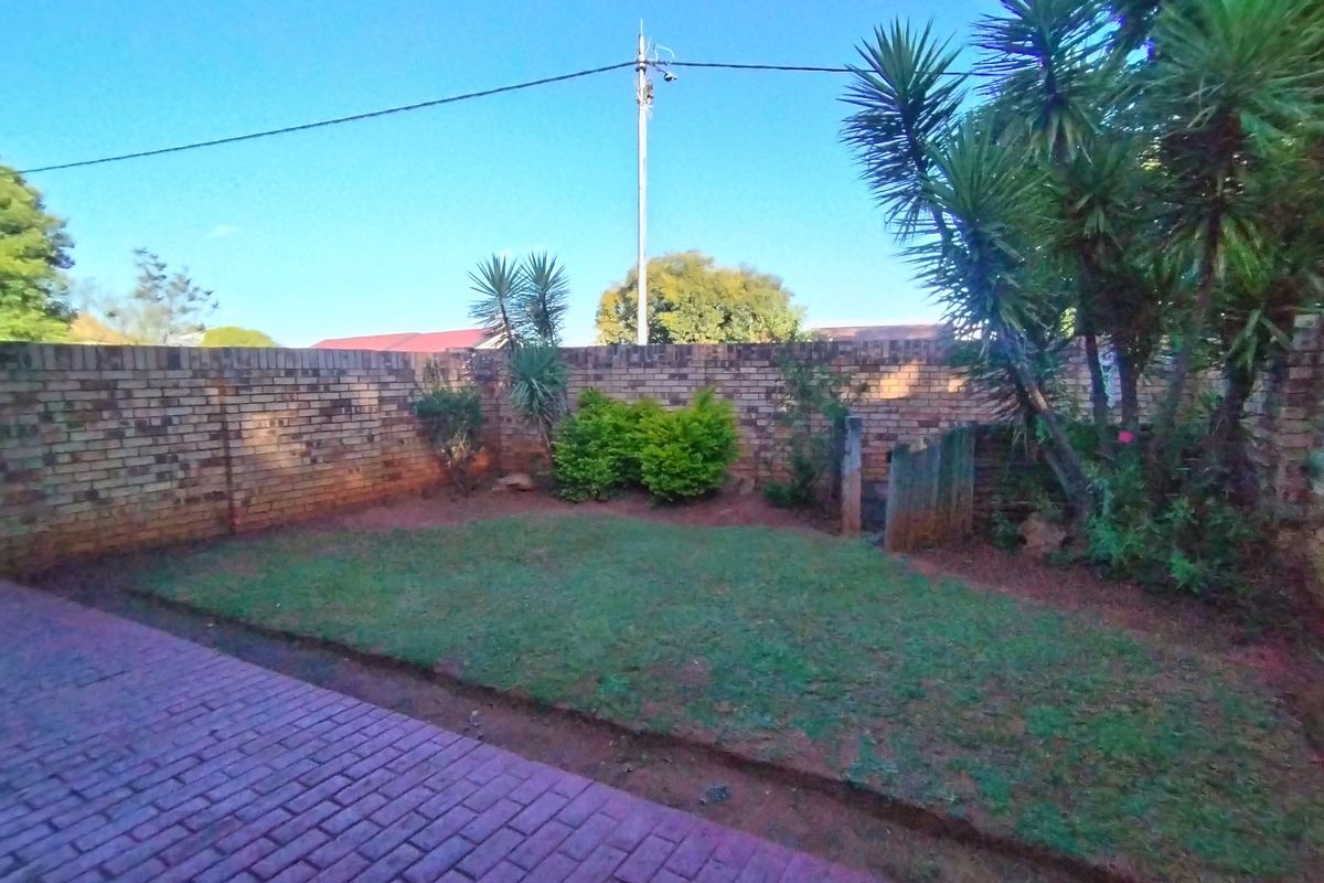 A private rear garden featuring a paved patio area, a small lawn, and a perimeter brick boundary wall.