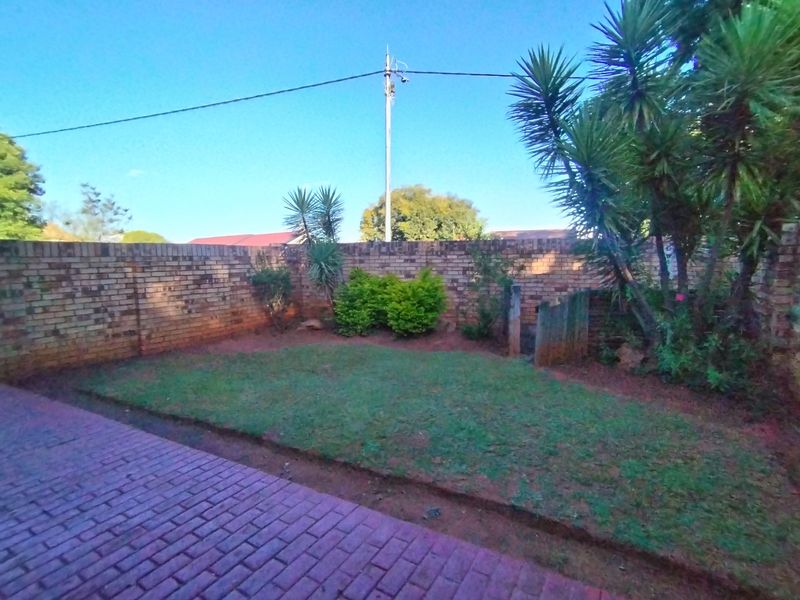 A private rear garden featuring a paved patio area, a small lawn, and a perimeter brick boundary wall.