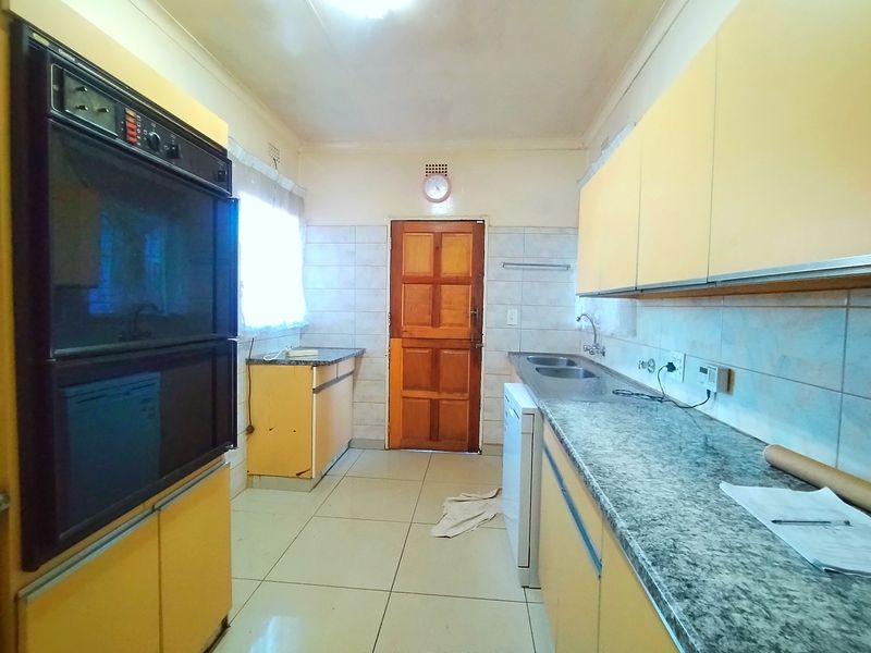 A functional kitchen featuring dated cabinetry, a built-in double oven, granite-look laminate countertops, and tiled flooring with direct access to an exterior door.