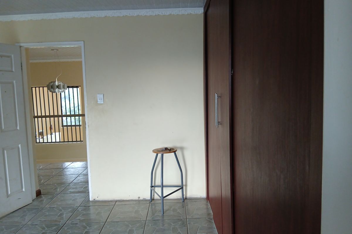 A bedroom interior featuring built-in wooden cupboards, tiled flooring, and a doorway leading to an adjacent room with security bars on the window.
