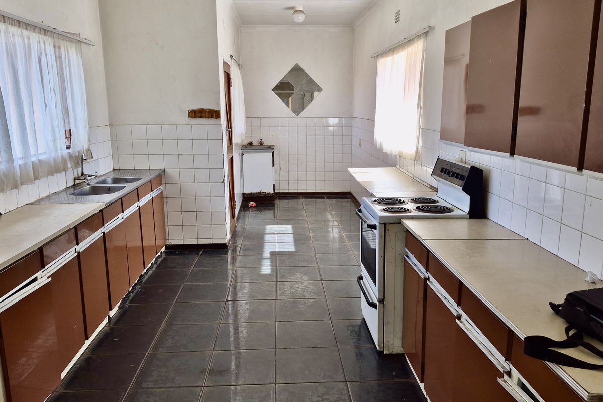 A dated galley-style kitchen featuring brown cabinetry, tiled splashbacks, and dark floor tiles, offering a functional layout ready for modernization.