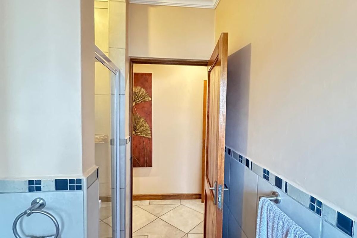 A functional bathroom featuring a glass-enclosed shower, tiled flooring, and wall-mounted towel fixtures, leading into an adjacent hallway.