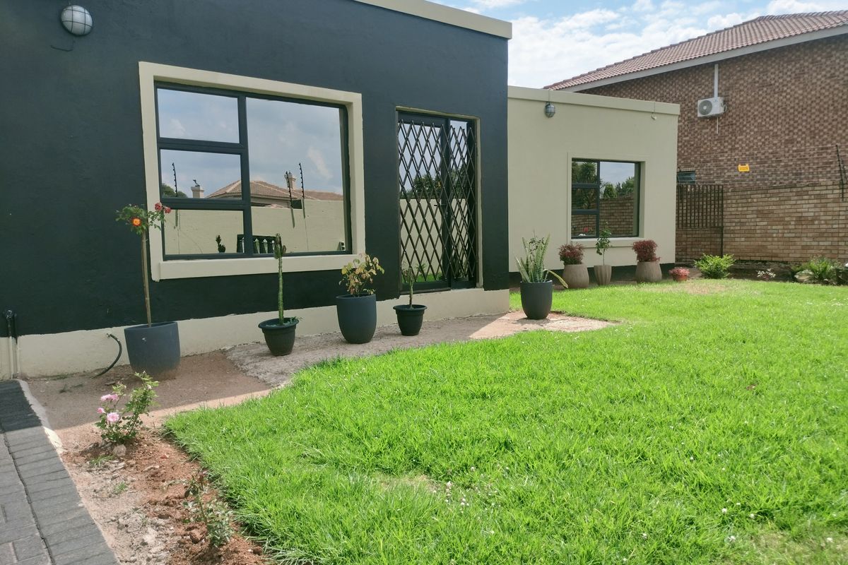 A view of the rear exterior of the house featuring a manicured lawn, paved walkway, and security gates on the windows and doors.
