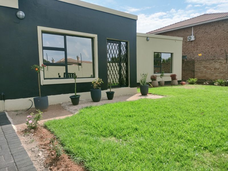 A view of the rear exterior of the house featuring a manicured lawn, paved walkway, and security gates on the windows and doors.