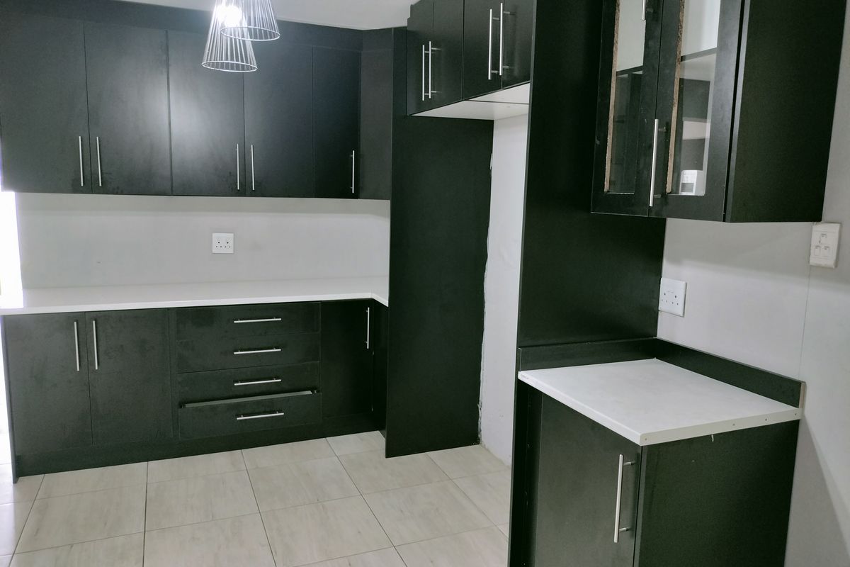 Modern kitchen featuring dark cabinetry, white countertops, and tiled flooring, offering a clean and functional workspace.