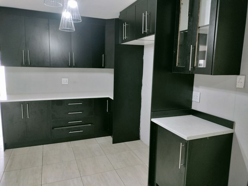 Modern kitchen featuring dark cabinetry, white countertops, and tiled flooring, offering a clean and functional workspace.
