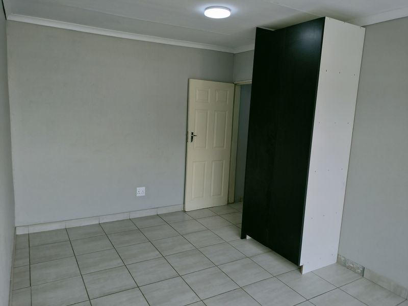 A simple bedroom featuring neutral grey walls, tiled flooring, and a built-in wardrobe.