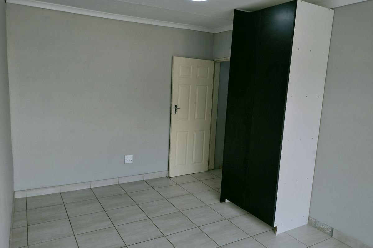A simple bedroom featuring neutral grey walls, tiled flooring, and a built-in wardrobe.