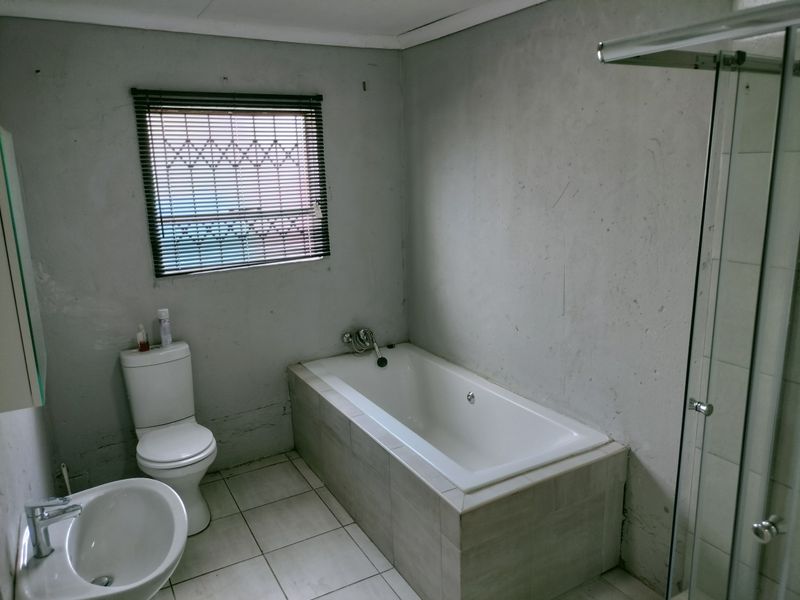 A functional bathroom featuring a built-in bathtub, separate shower enclosure, pedestal basin, and toilet, currently requiring cosmetic wall finishing.