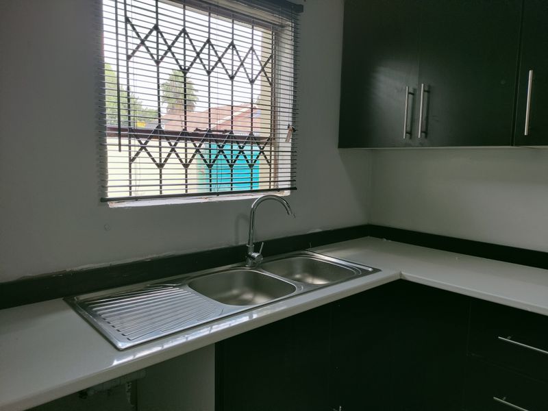 A functional kitchen area featuring dark cabinetry, white countertops, a stainless steel double sink, and a window with security bars.