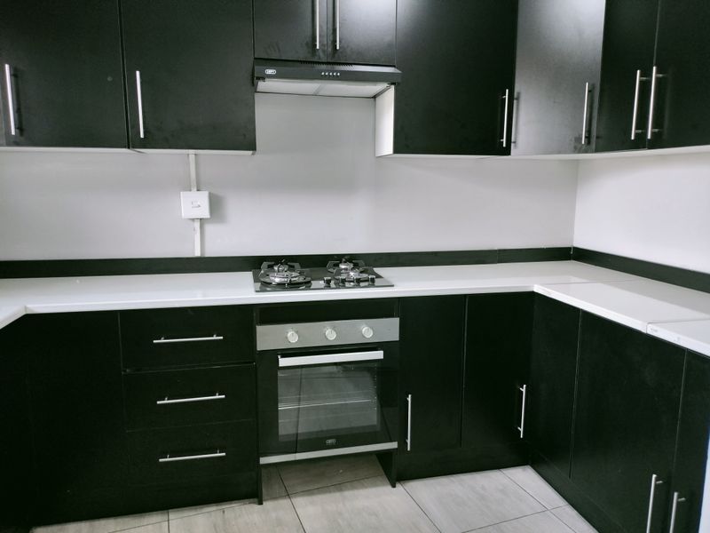 Modern kitchen featuring black cabinetry, white countertops, built-in oven, gas hob, and extractor fan.